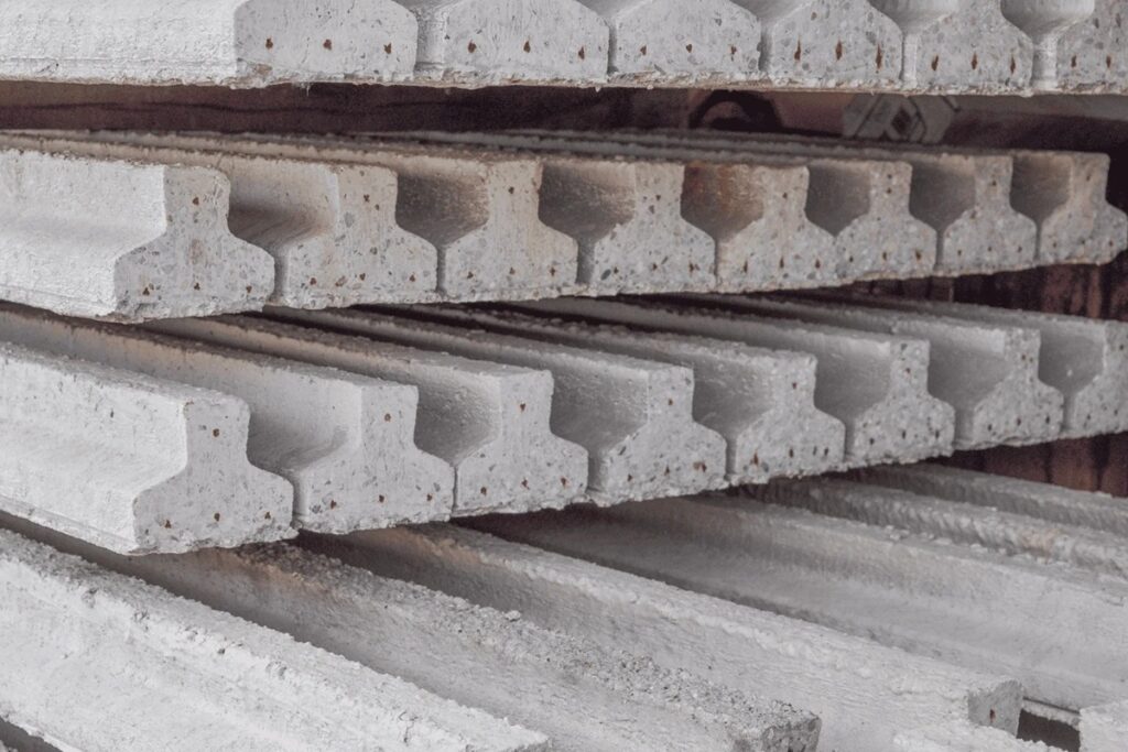 Vigas de concreto pré-moldado empilhadas horizontalmente, com formato estrutural padronizado, prontas para aplicação na construção civil.