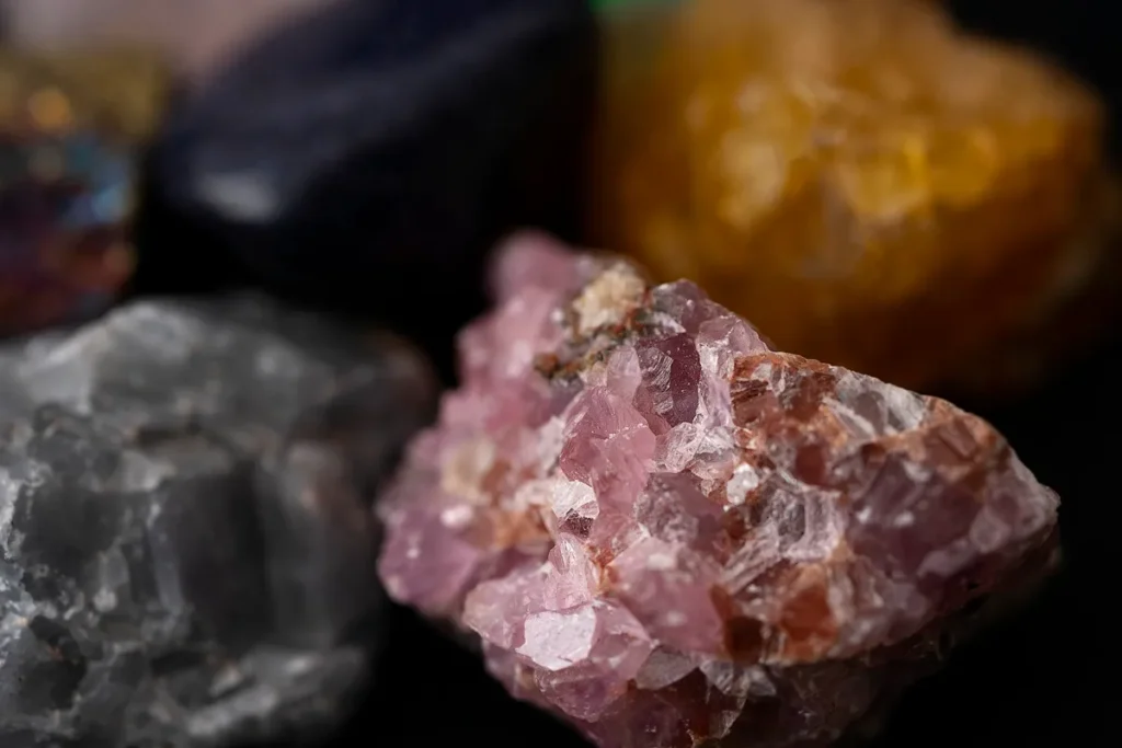 Minerais coloridos em estado bruto, com cristais rosados e rochas naturais ao fundo