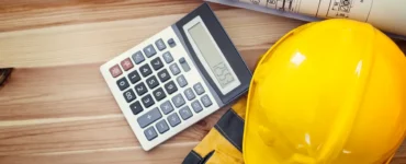 Capacete de segurança amarelo, luvas de proteção, calculadora e planta arquitetônica sobre mesa de madeira, representando orçamento e planejamento de obras.