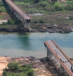 Ponte parcialmente destruída sobre rio com nível de água baixo, evidenciando efeitos da seca extrema