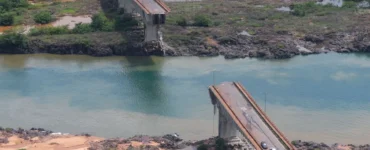 Ponte parcialmente destruída sobre rio com nível de água baixo, evidenciando efeitos da seca extrema