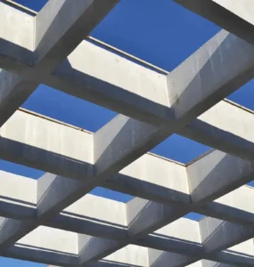 Estrutura de vigas de concreto armado dispostas em formato geométrico, formando uma grelha vazada com o céu azul ao fundo.