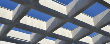 Estrutura de vigas de concreto armado dispostas em formato geométrico, formando uma grelha vazada com o céu azul ao fundo.