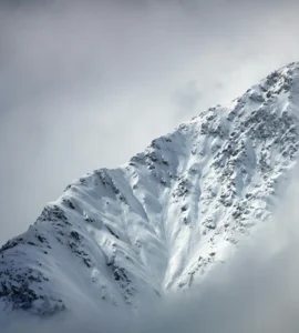 Montanha coberta de neve parcialmente envolta por nuvens em uma região fria de alta altitude.
