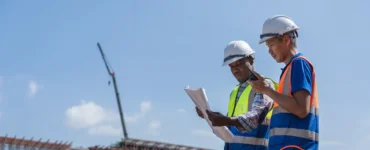 dois profissionais de construção com capacete analisando documento em obra ao ar livre