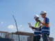 dois profissionais de construção com capacete analisando documento em obra ao ar livre