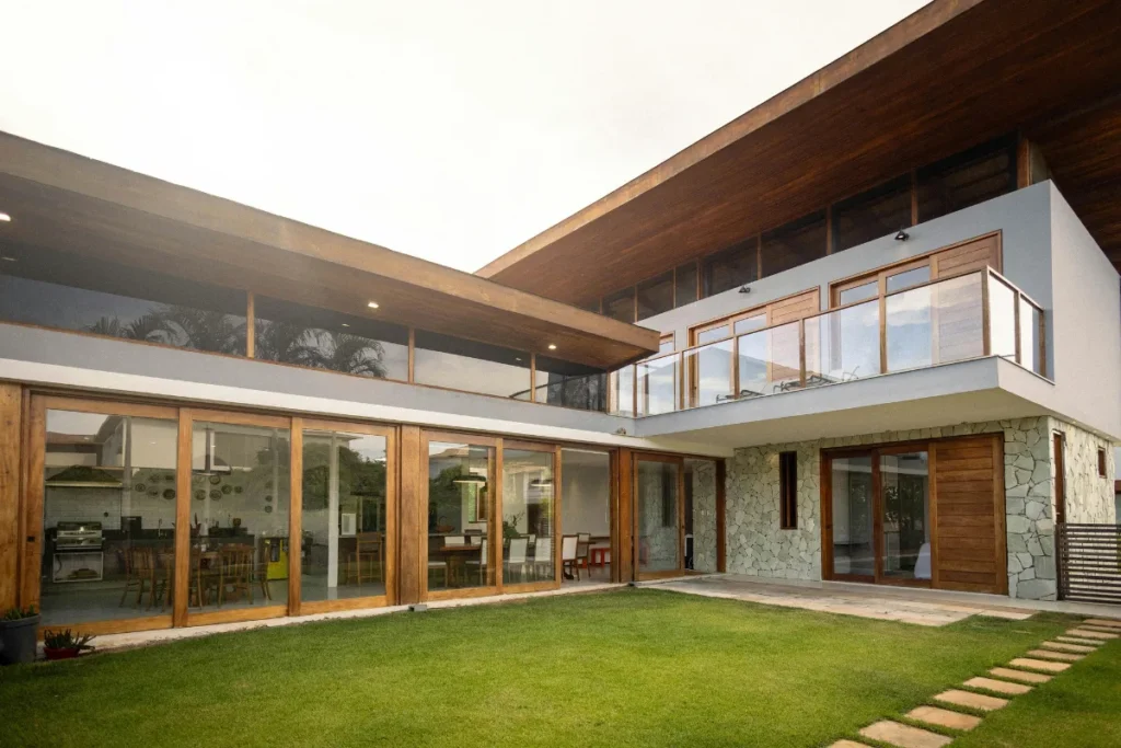 Casa moderna com grandes portas de vidro, estrutura em madeira e área verde no jardim.