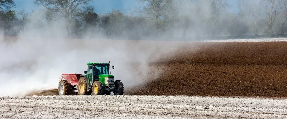 Trator espalhando material branco no solo agrícola durante preparo da terra