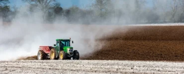 Trator espalhando material branco no solo agrícola durante preparo da terra