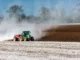 Trator espalhando material branco no solo agrícola durante preparo da terra