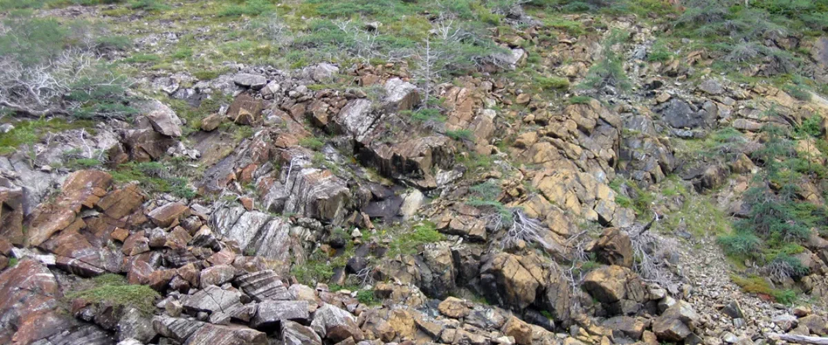Encosta rochosa com diferentes blocos de pedra e vegetação espalhada em uma paisagem natural.
