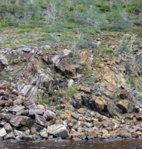Encosta rochosa com diferentes blocos de pedra e vegetação espalhada em uma paisagem natural.