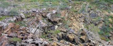 Encosta rochosa com diferentes blocos de pedra e vegetação espalhada em uma paisagem natural.