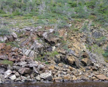 Encosta rochosa com diferentes blocos de pedra e vegetação espalhada em uma paisagem natural.