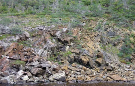 Encosta rochosa com diferentes blocos de pedra e vegetação espalhada em uma paisagem natural.