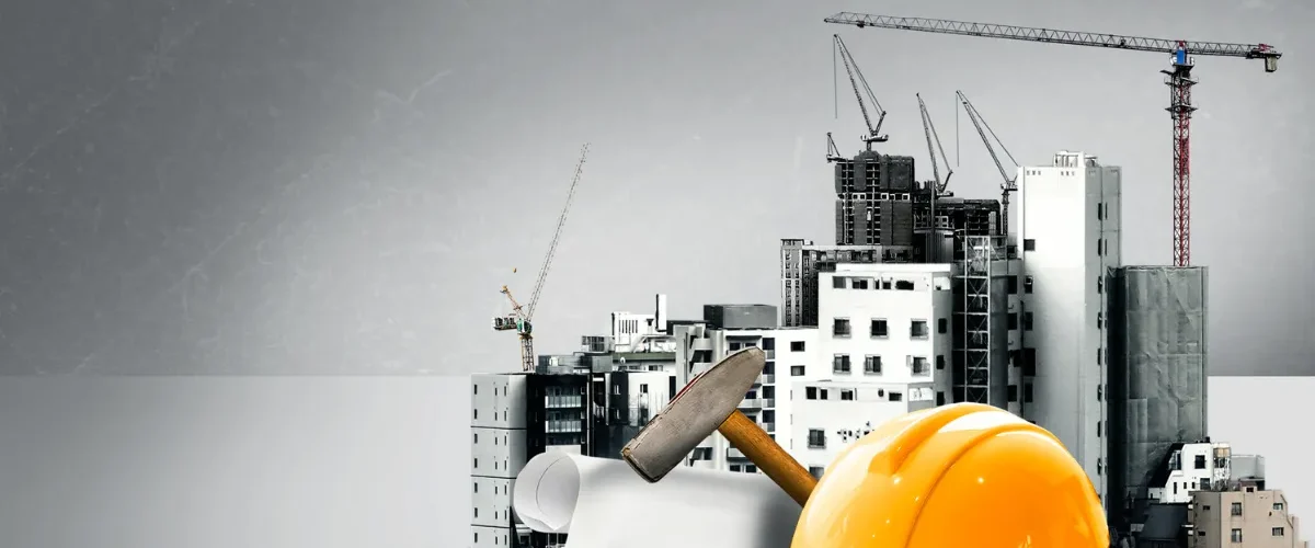 Capacete de segurança amarelo, martelo e plantas de projeto diante de prédios em construção com guindastes.