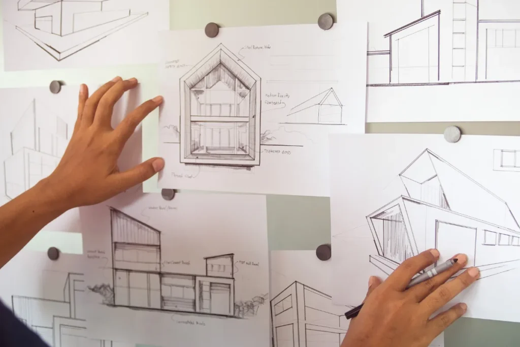 Mão organizando vários esboços arquitetônicos de casas fixados em uma parede