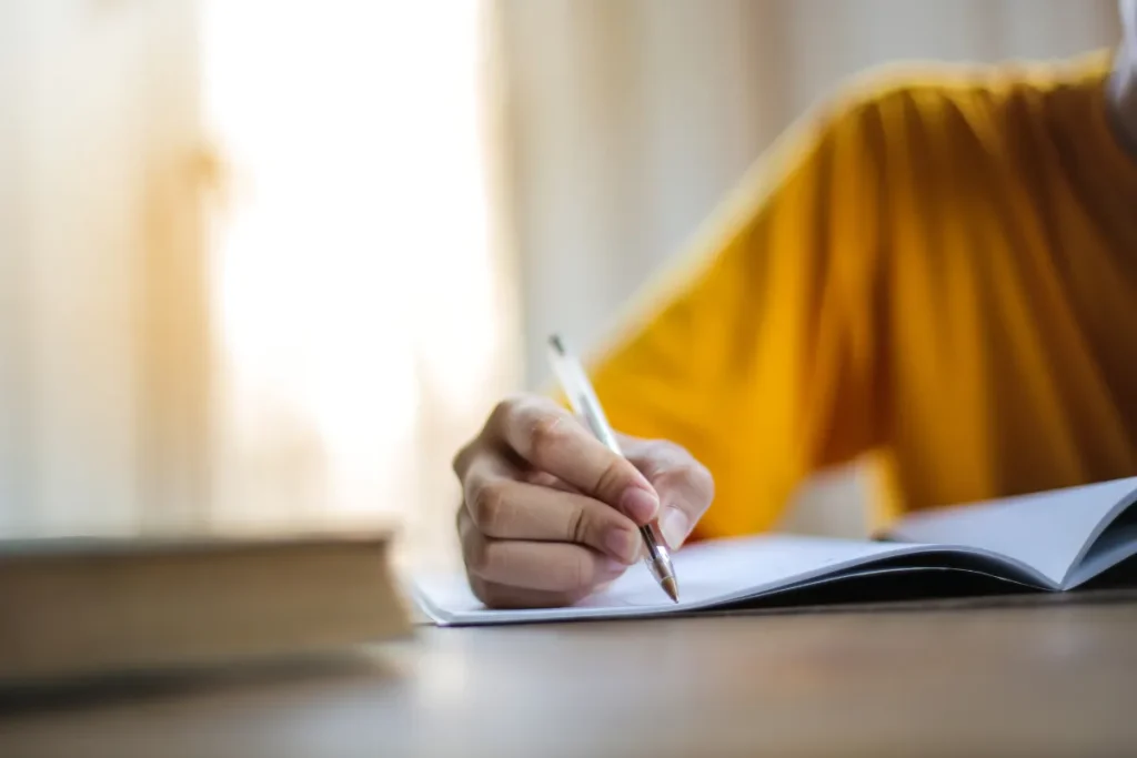 mão segurando caneta escrevendo em caderno aberto com foco no movimento da escrita
