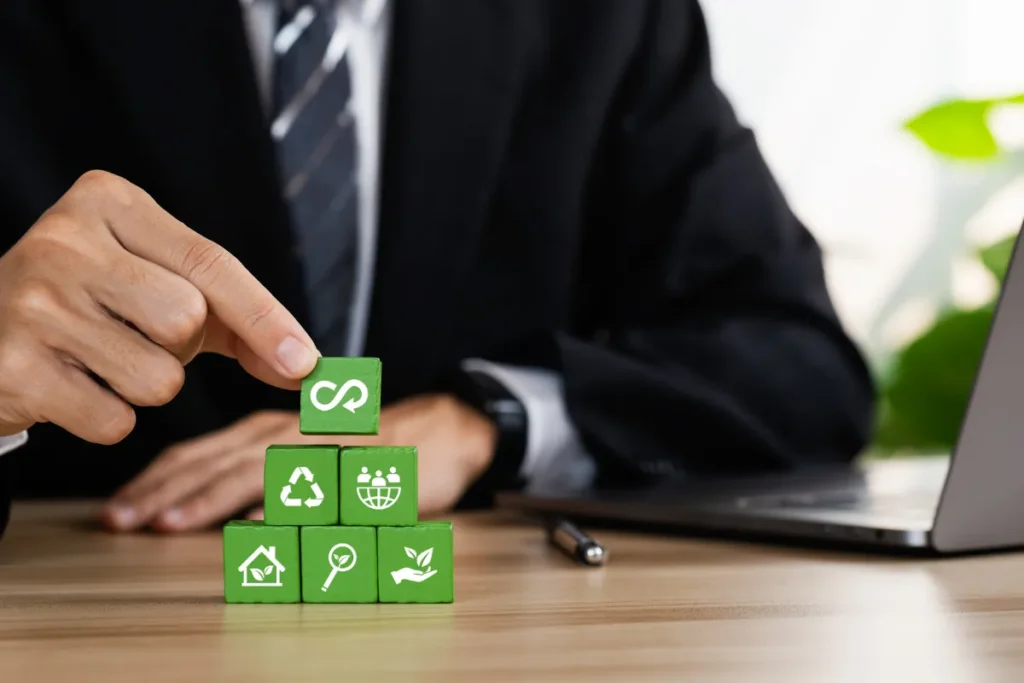 Pessoa empilhando blocos verdes com ícones de reciclagem, energia limpa e sustentabilidade sobre uma mesa.