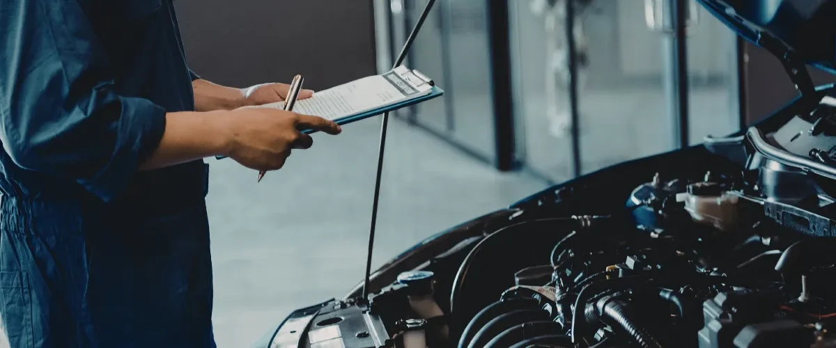 mecânico analisando motor de carro com capô aberto enquanto segura prancheta